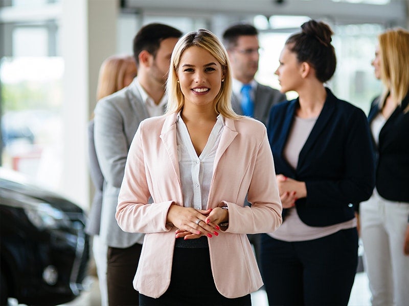 Professionally dressed women among other people at a car dealership